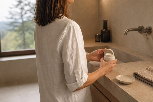 Frau hält am Lavabo ein geöffnetes Cremetöpfchen, Blick über die Schulter